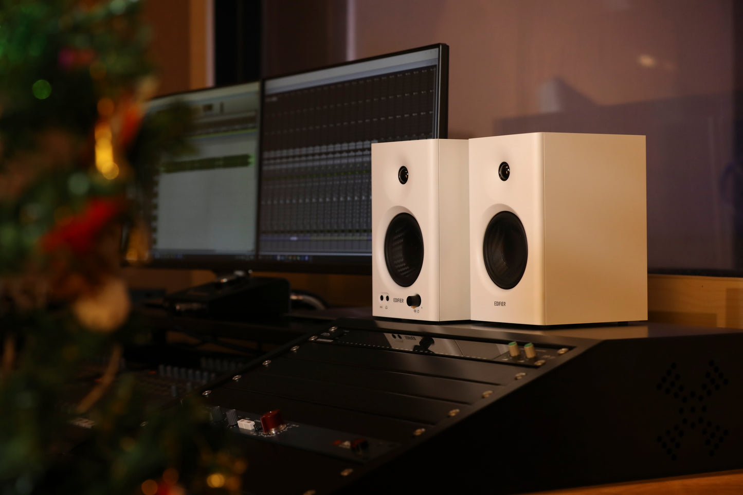 Monitores Edifier MR4 blancos junto a consola en un estudio con decoración navideña.