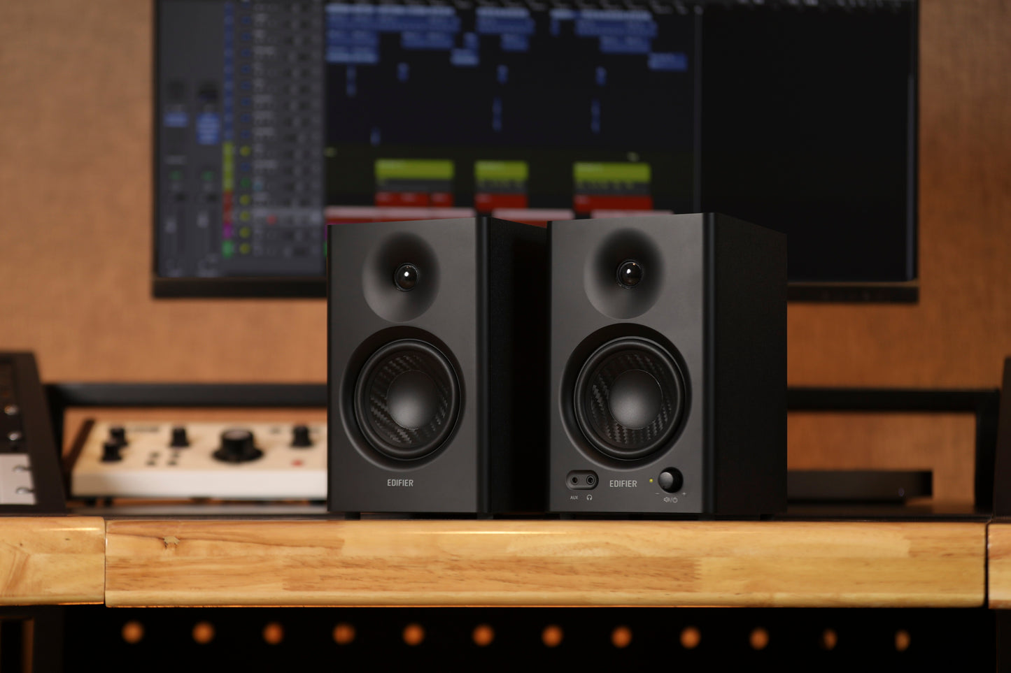 Monitores Edifier MR4 en negro sobre escritorio frente a estación de mezcla de audio.