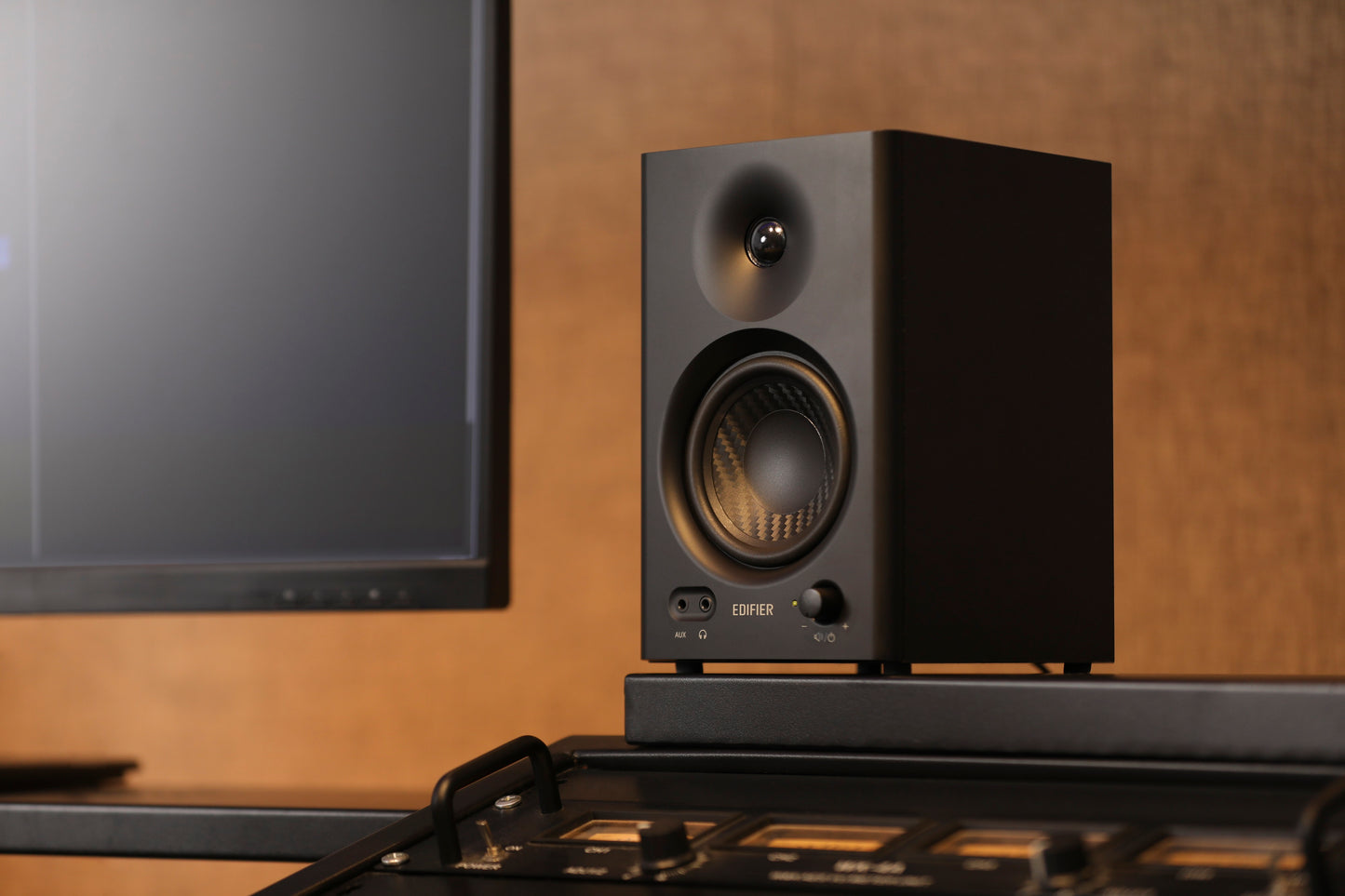 Vista lateral en detalle del monitor Edifier MR4 negro junto a consola de mezcla y monitor.