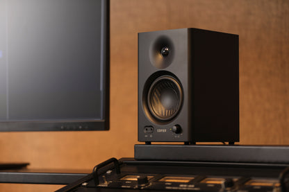 Vista lateral en detalle del monitor Edifier MR4 negro junto a consola de mezcla y monitor.